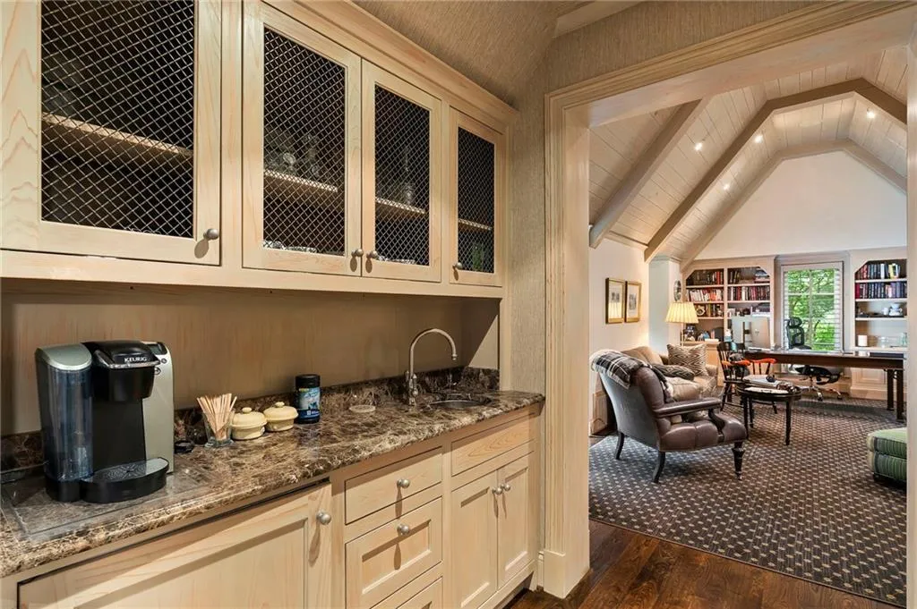 Built-in wet bar featuring custom cabinetry with wire mesh inserts, stone countertop, and undermount sink