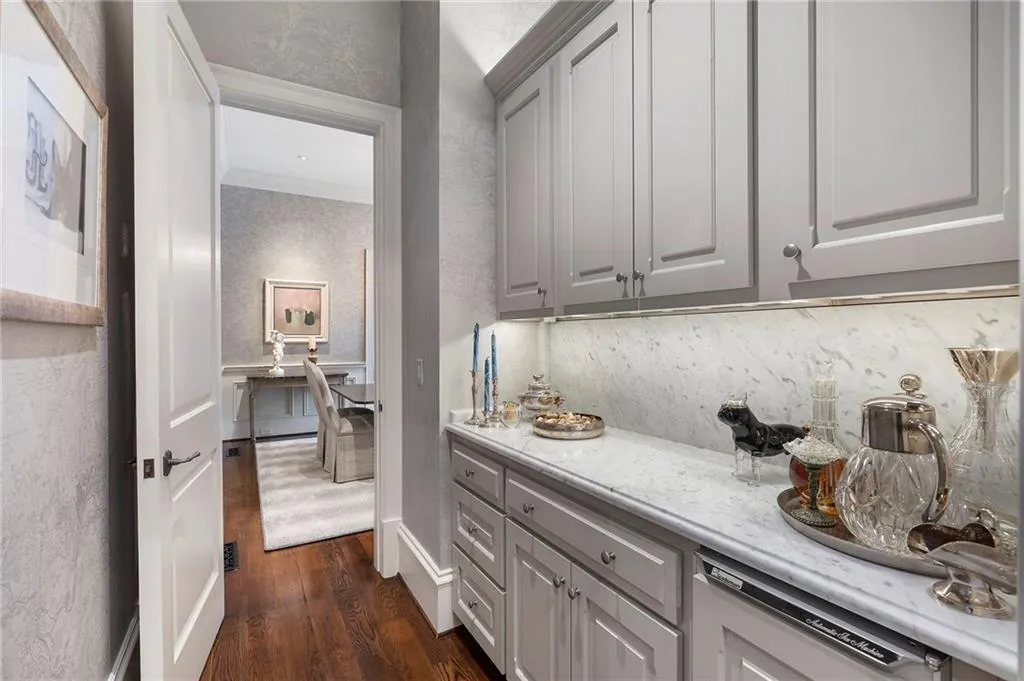 Hallway wet bar featuring light gray cabinetry, a white stone countertop, a matching stone backsplash, and under-cabinet lighting