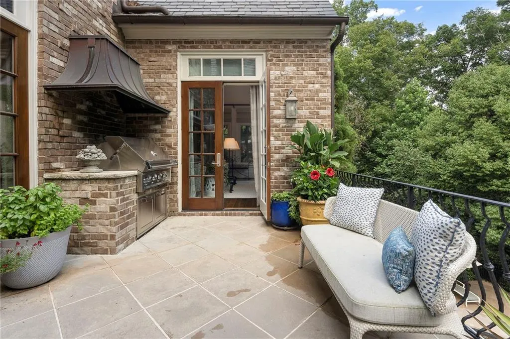 Outdoor patio featuring stone tile flooring, a built-in brick grilling station with a stainless steel grill and range hood, and double glass-paneled doors