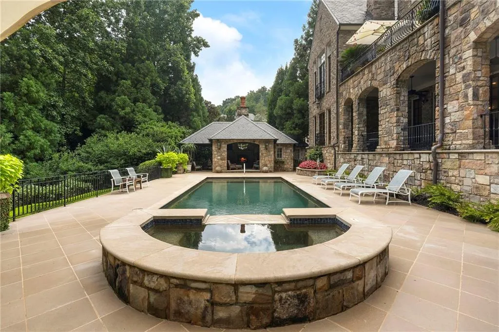 Stone exterior featuring an integrated pool and raised spa, expansive patio with natural stone pavers, and a detached stone pool house