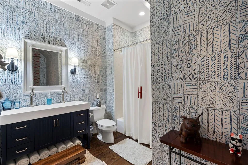 Bathroom featuring patterned wallpaper, a dark wood-finish vanity with a white countertop, a framed mirror, and two sconces