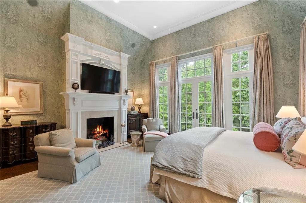 Formal bedroom featuring an ornate white fireplace mantel, high ceilings, and patterned wallpaper