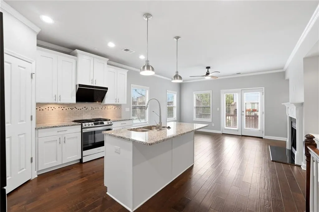 Kitchen with a kitchen island with sink, stainless steel gas stove, white cabinetry, ornamental molding, and light stone countertops