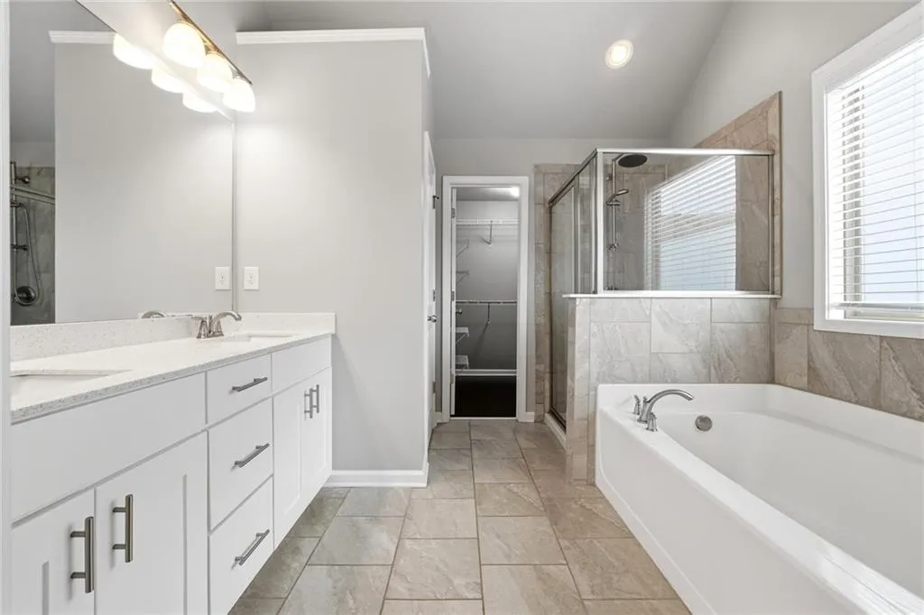 Full bath with a shower stall, double vanity, a bath, a spacious closet, and vaulted ceiling