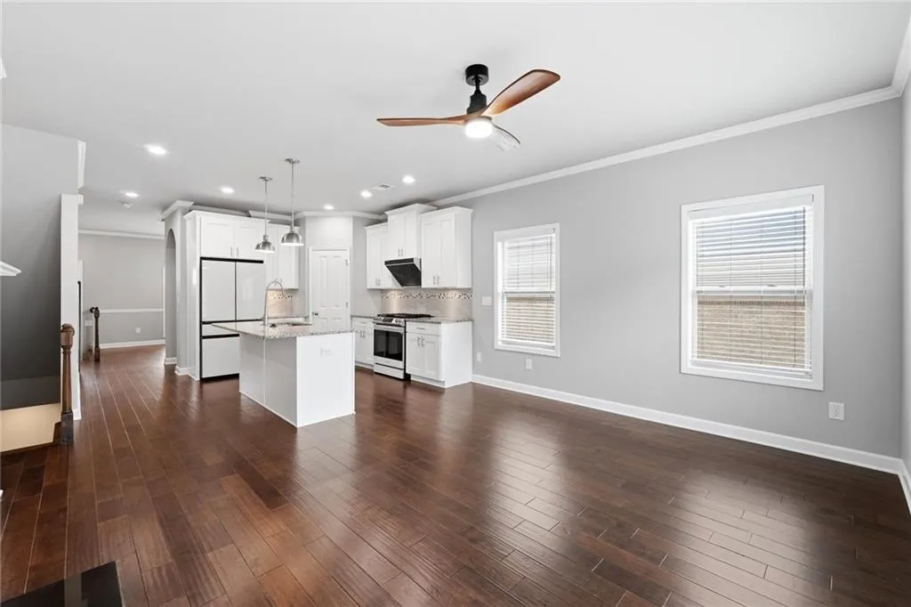 Kitchen with a kitchen island with sink, white cabinets, ceiling fan, dark wood-style flooring, and ornamental molding