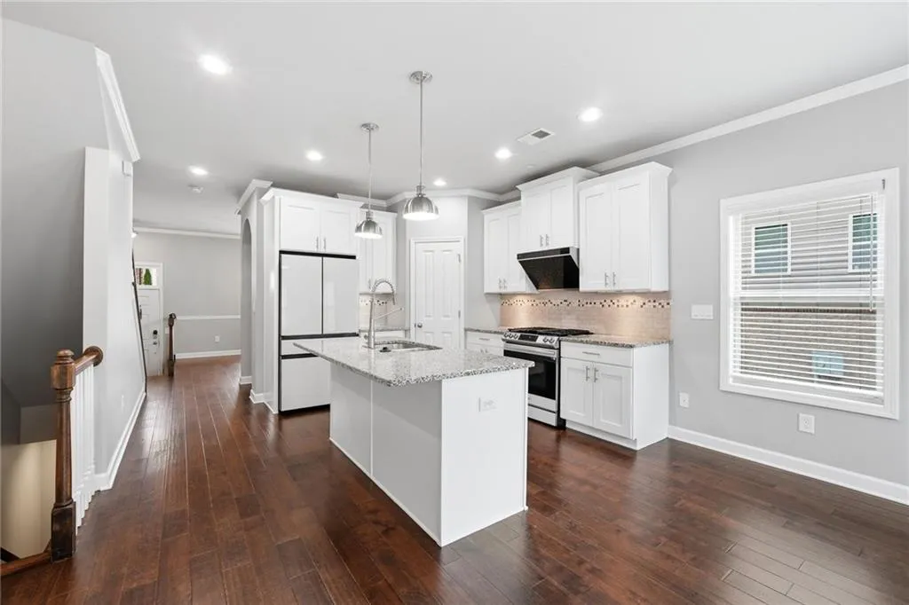 Kitchen with white cabinetry, gas stove, dark wood-type flooring, freestanding refrigerator, and ornamental molding
