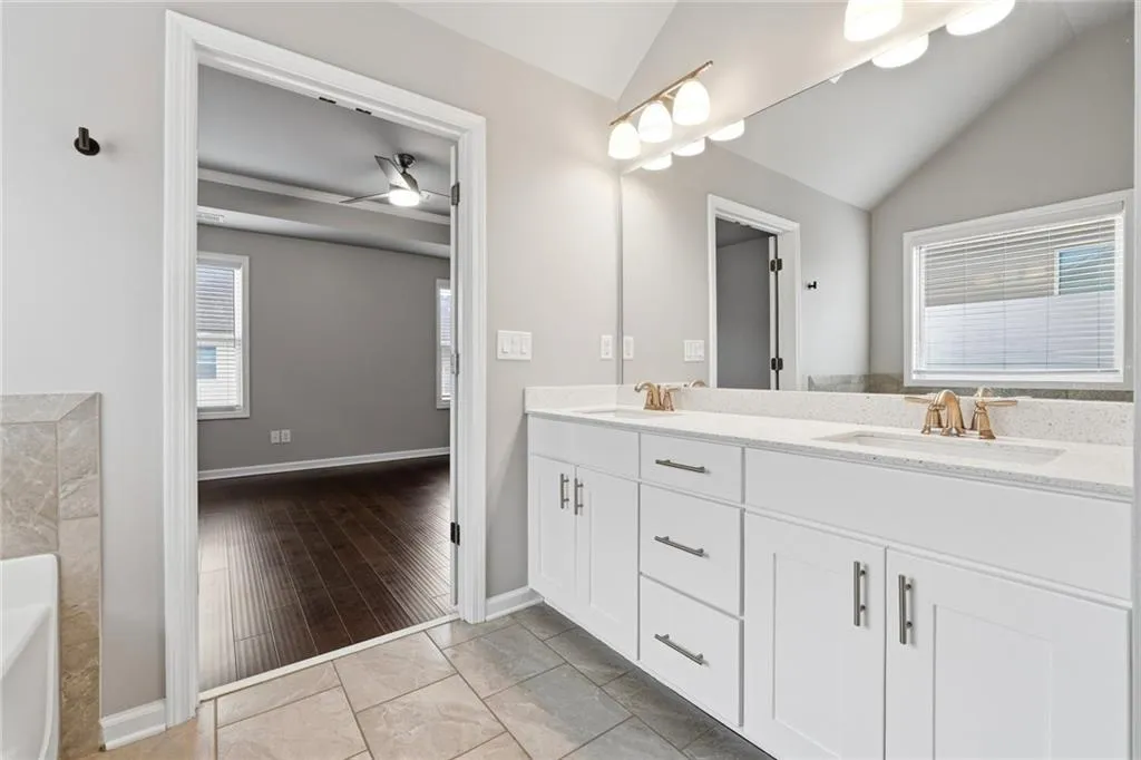 Full bathroom with double vanity, a ceiling fan, lofted ceiling, a bath, and plenty of natural light