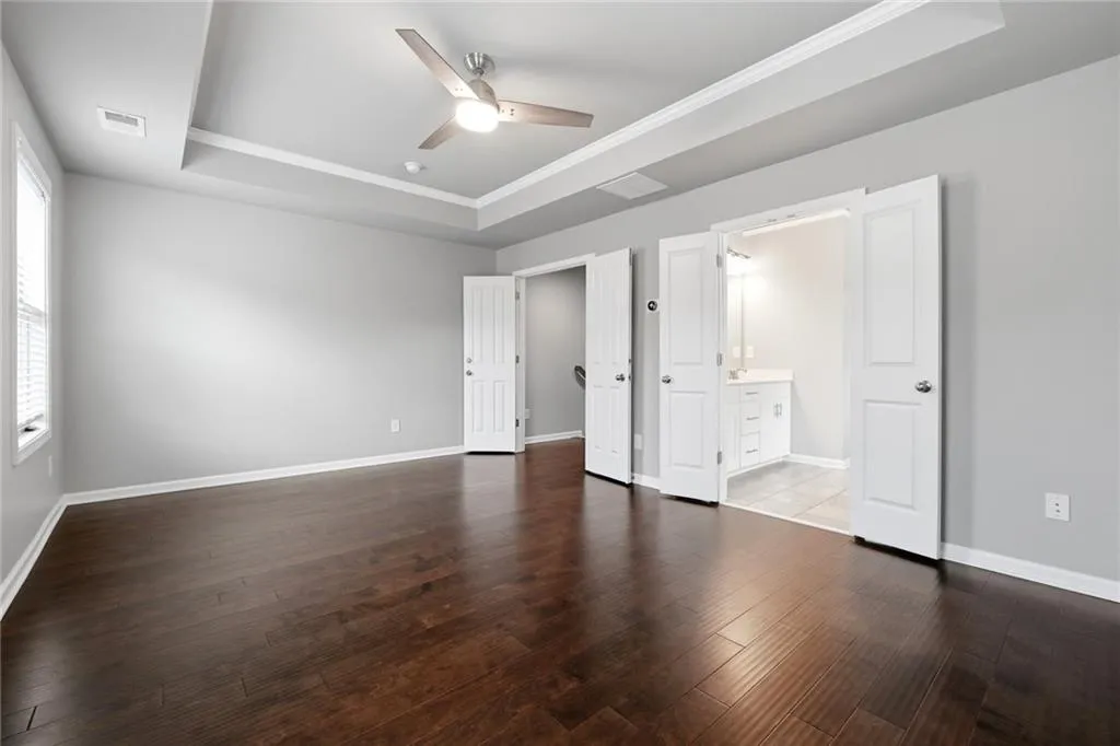 Unfurnished bedroom featuring a raised ceiling, ceiling fan, dark wood-style floors, ornamental molding, and ensuite bathroom