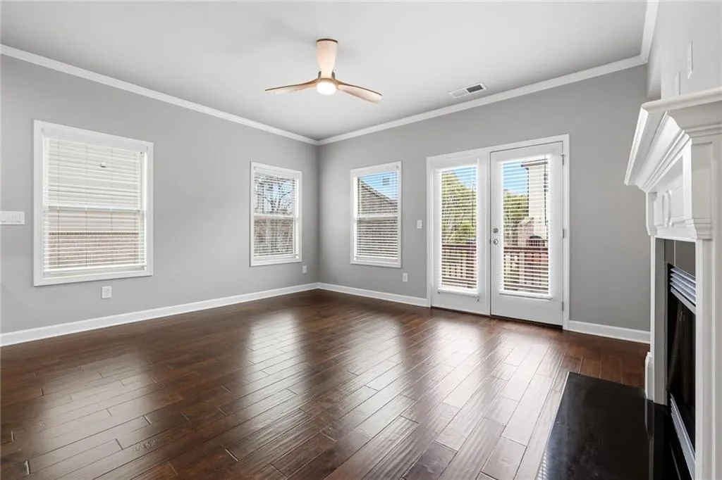 Unfurnished living room featuring ceiling fan, a fireplace, dark wood-style floors, crown molding, and french doors