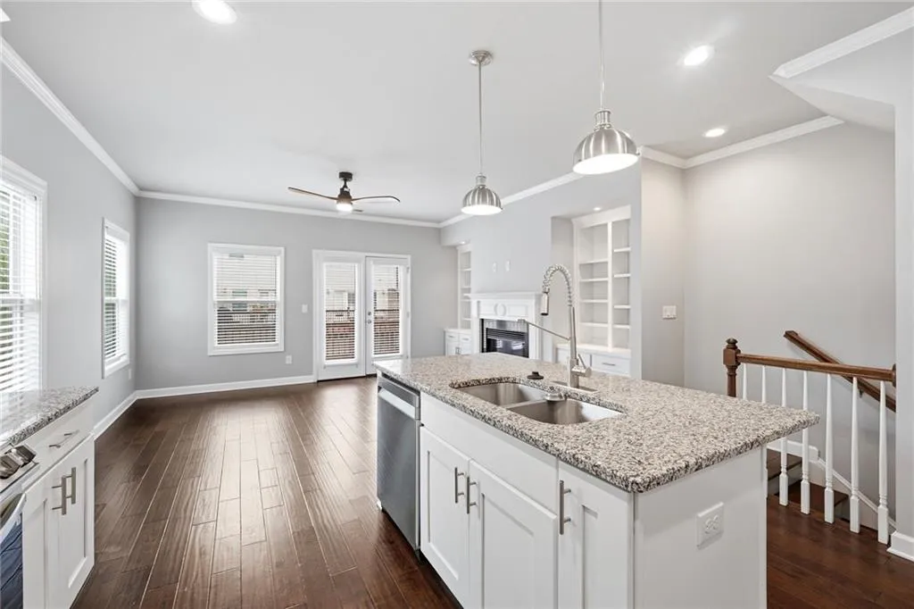 Kitchen with light stone counters, white cabinets, dark wood-style flooring, a glass covered fireplace, and ornamental molding