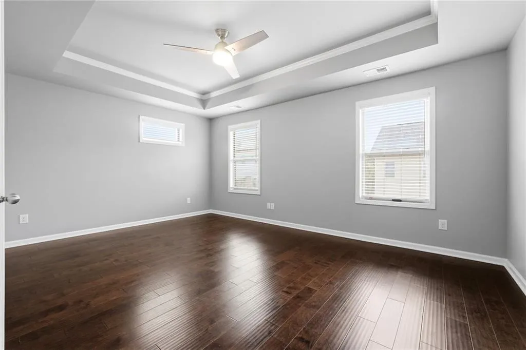 Unfurnished room with ceiling fan, a tray ceiling, ornamental molding, and dark wood finished floors