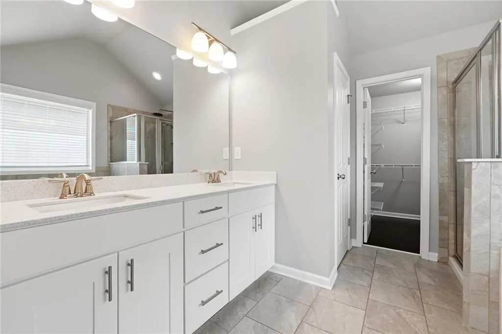 Bathroom with double vanity, a stall shower, a spacious closet, and vaulted ceiling