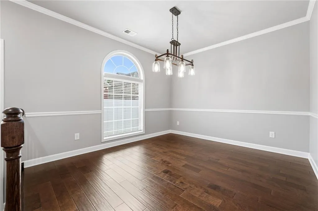 Unfurnished room with ornamental molding, dark wood-type flooring, and suspended lighting