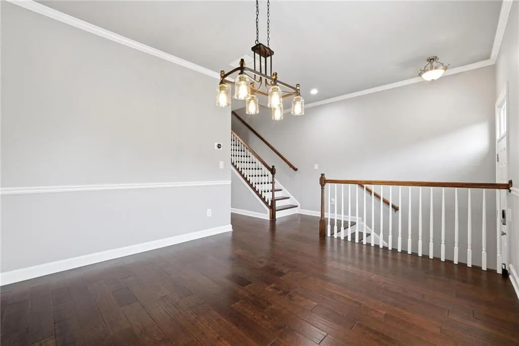 Empty room featuring crown molding, dark wood-type flooring, and a chandelier