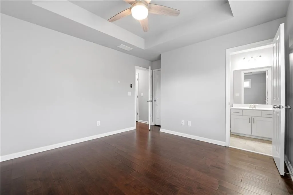 Unfurnished bedroom featuring a raised ceiling, dark wood finished floors, a ceiling fan, and ensuite bathroom