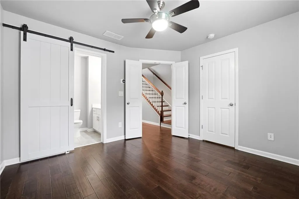 Unfurnished bedroom featuring a barn door, a ceiling fan, connected bathroom, and dark wood-type flooring