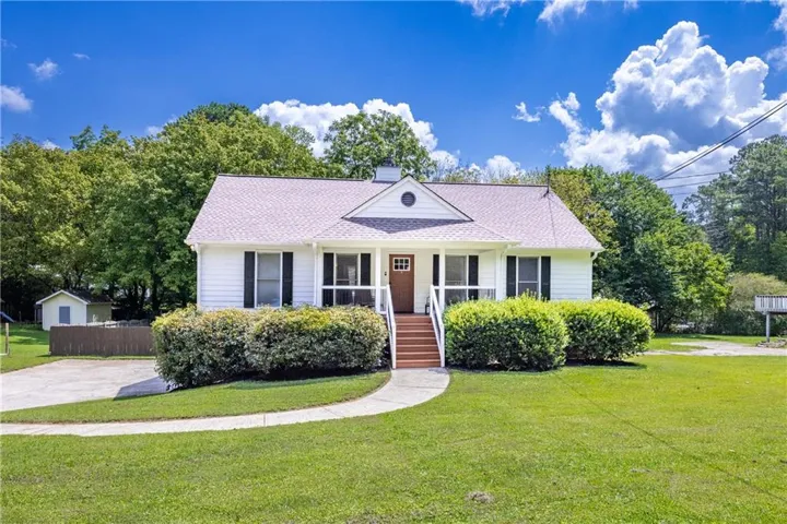White exterior siding with dark shutters, front porch with wood-finish steps, established front yard landscaping, and a paved driveway