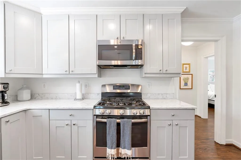 Kitchen featuring crown molding, dark hardwood / wood-style flooring, stainless steel appliances, light stone countertops, and white cabinetry