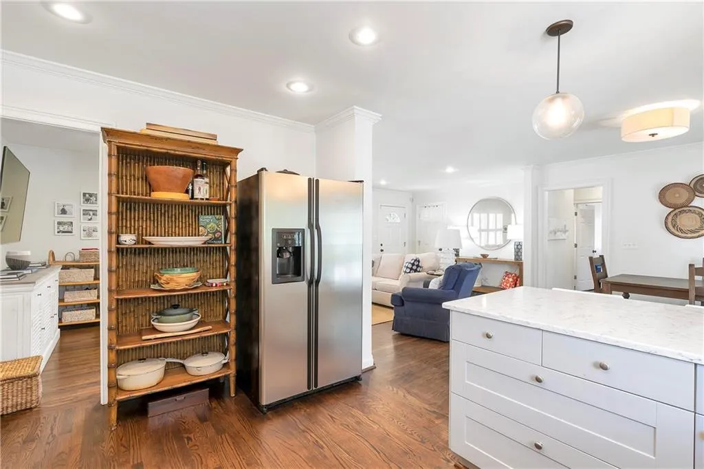Kitchen featuring pendant lighting, light stone counters, stainless steel fridge with ice dispenser, ornamental molding, and dark wood-type flooring