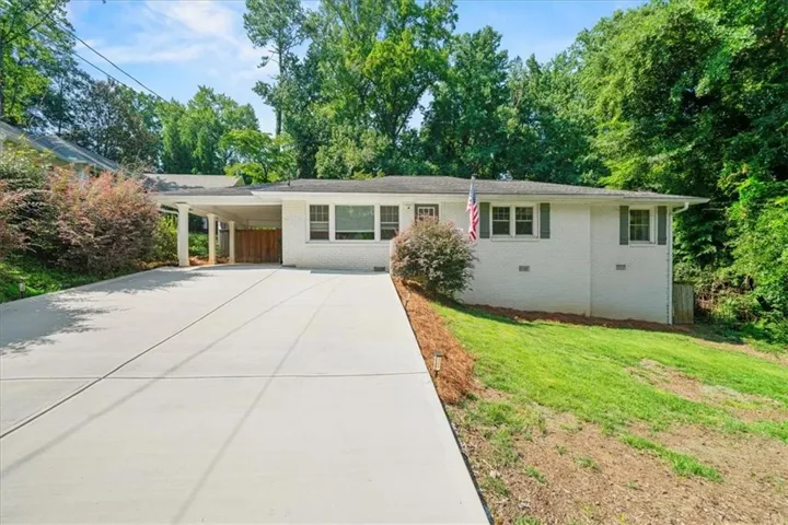 White brick exterior with a flat roofline, featuring a carport and an extended concrete driveway