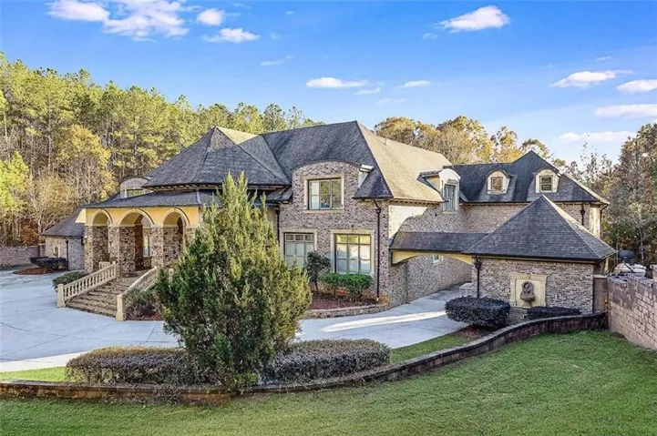 Stone and brick exterior featuring a multi-level roofline, arched portico, stone balustrade, and a covered driveway leading to an integrated garage