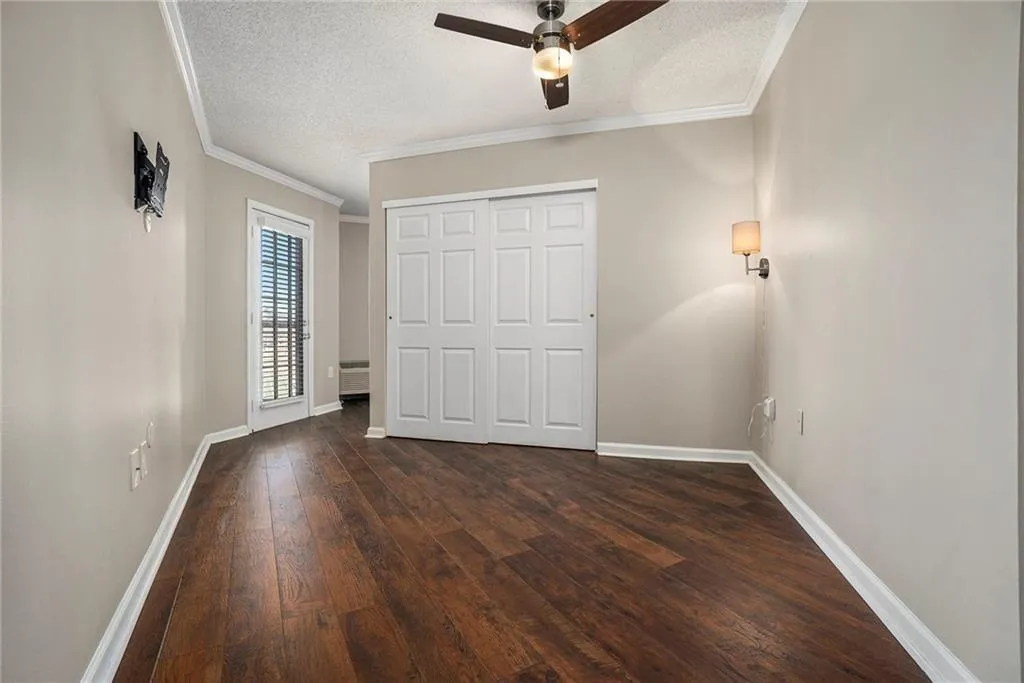 Unfurnished bedroom featuring a textured ceiling, ornamental molding, dark hardwood / wood-style flooring, a closet, and ceiling fan