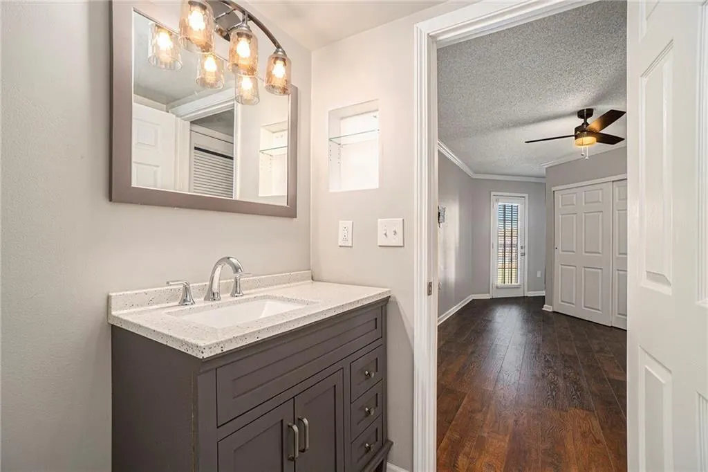 Bathroom with crown molding, a textured ceiling, ceiling fan with notable chandelier, hardwood / wood-style flooring, and vanity