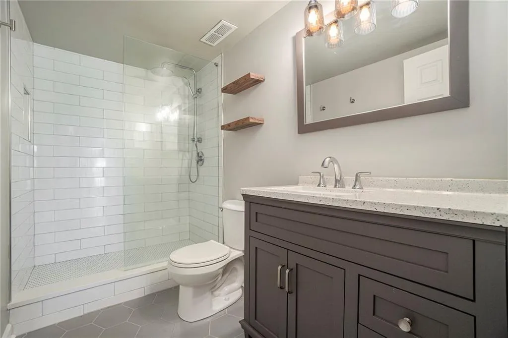 Bathroom featuring vanity with extensive cabinet space, walk in shower, tile flooring, and toilet
