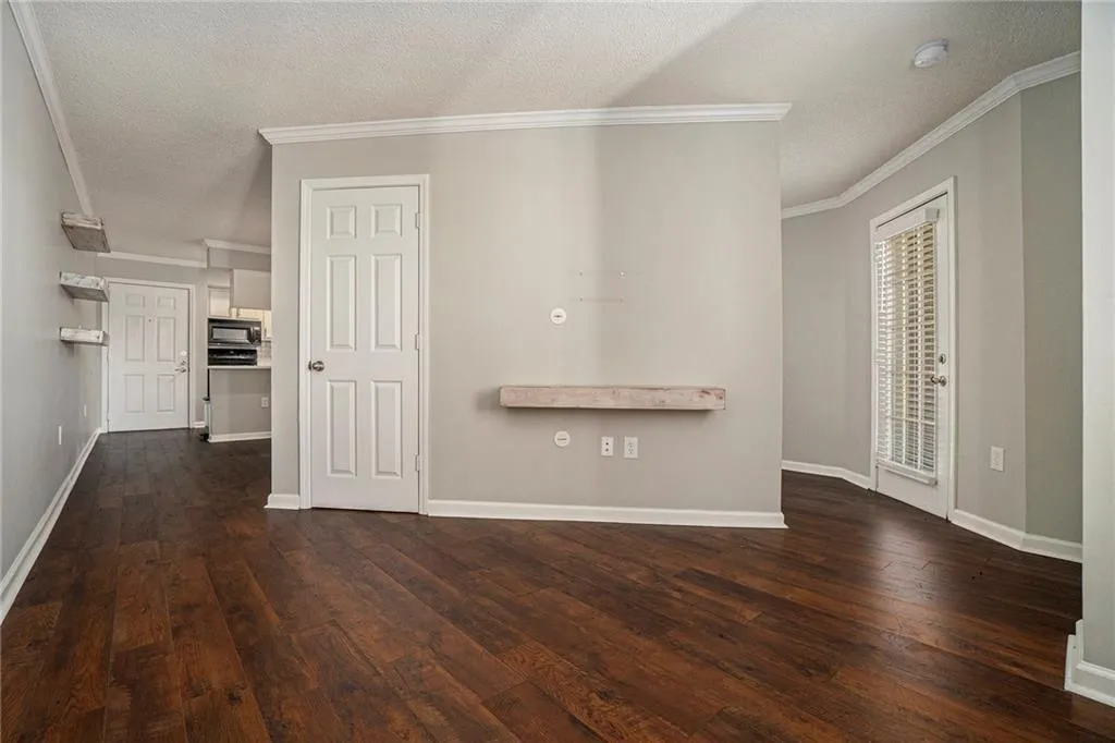 Unfurnished living room featuring dark wood-type flooring, a textured ceiling, and crown molding