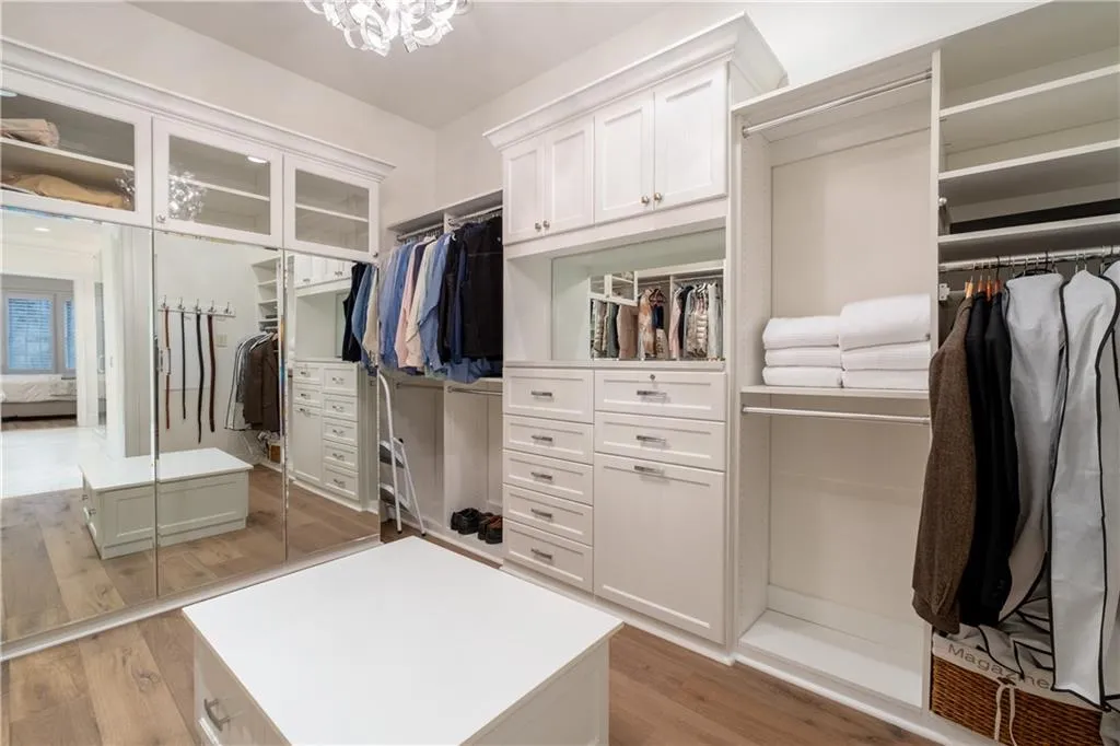 Spacious custom closet with an inviting chandelier , lots of hanging and storage space and hardwood floors