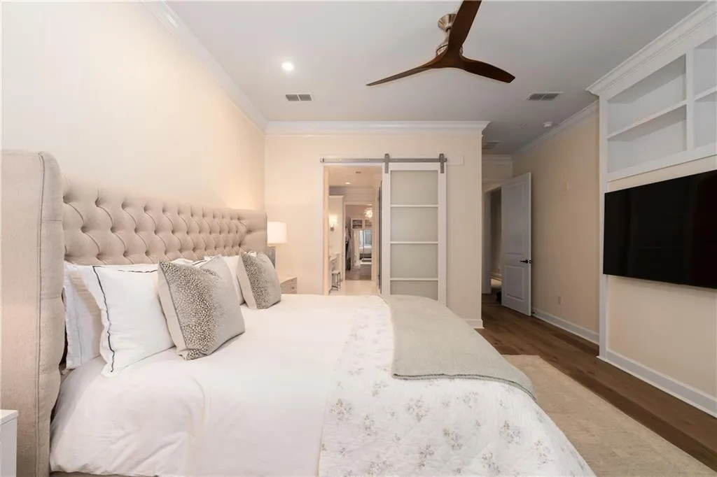 Bedroom ensuite bathroom, dark hardwood / wood-style flooring, ornamental molding, a barn door, and ceiling fan