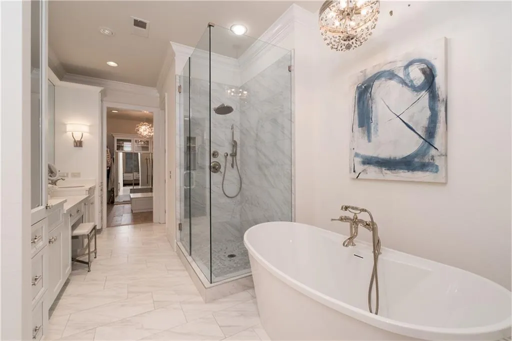 Spa-like Bathroom with plus walk in shower, ornamental molding, a notable chandelier, vanity, and marble/ tile flooring, and relaxing soaking tub