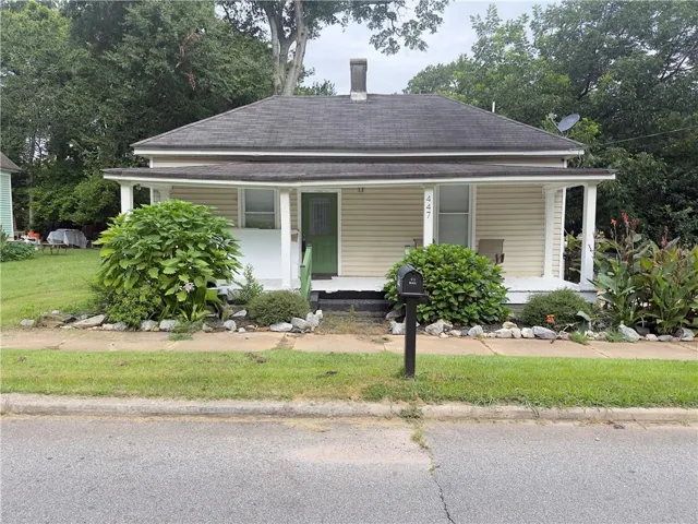 Traditional-style home featuring a covered front porch with white pillars, light-colored siding, and a dark shingle roof