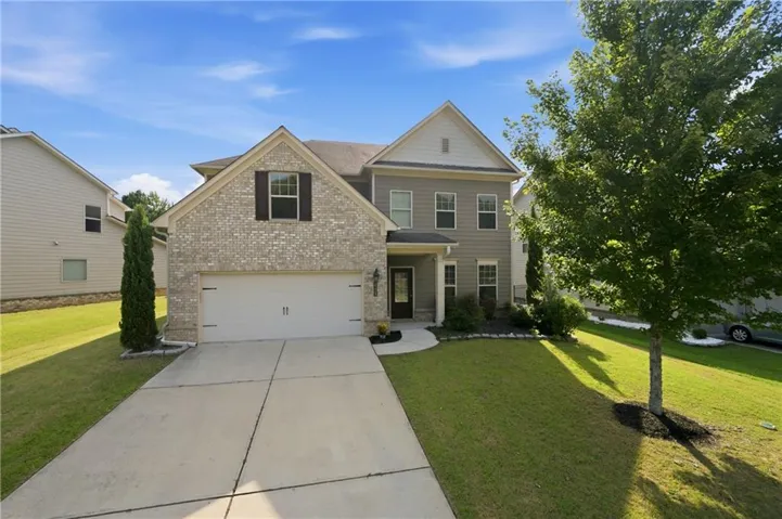Two-story residence featuring a brick and siding exterior, an attached garage, a concrete driveway, and established landscaping