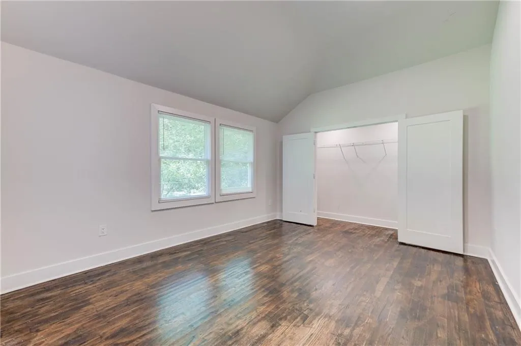 Unfurnished bedroom with dark wood-type flooring, lofted ceiling, and a closet