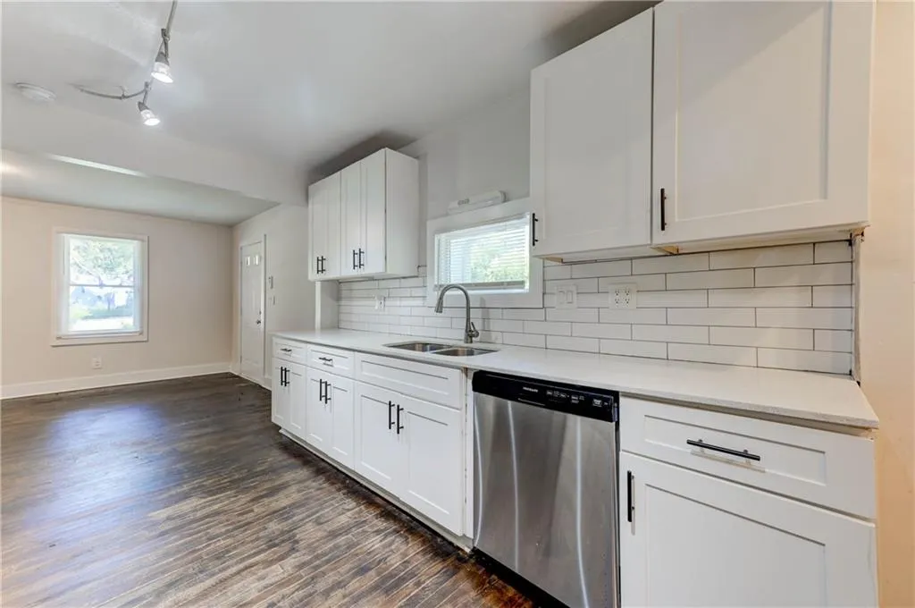 Kitchen with dishwasher, dark wood-style floors, track lighting, light countertops, and backsplash