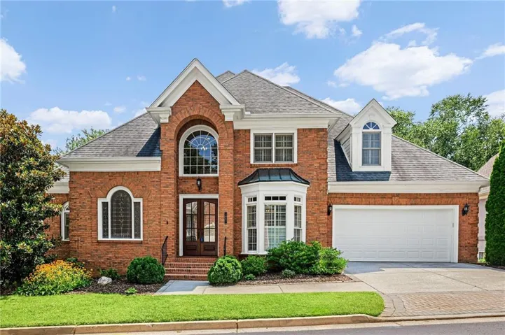 Brick exterior residence featuring a prominent arched window above double entry doors, a bay window, and a two-car garage