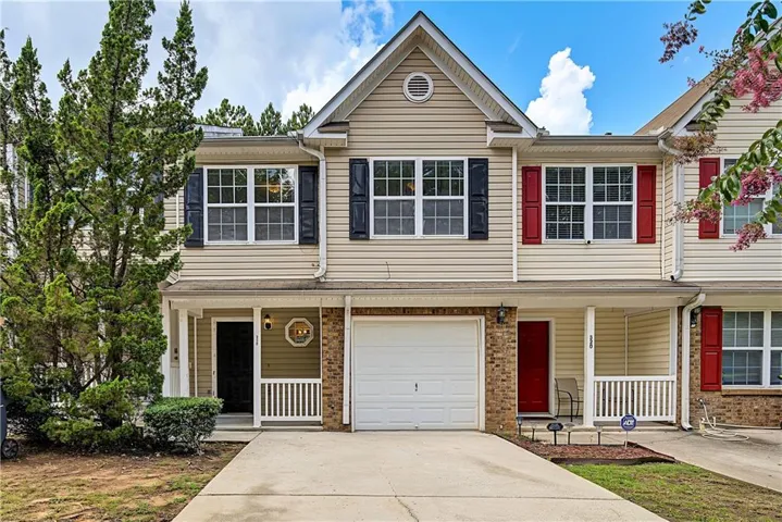 Charming two-story townhome featuring a brick and siding exterior with black-shuttered windows, a covered front entry with white railings, and an attached single-car garage