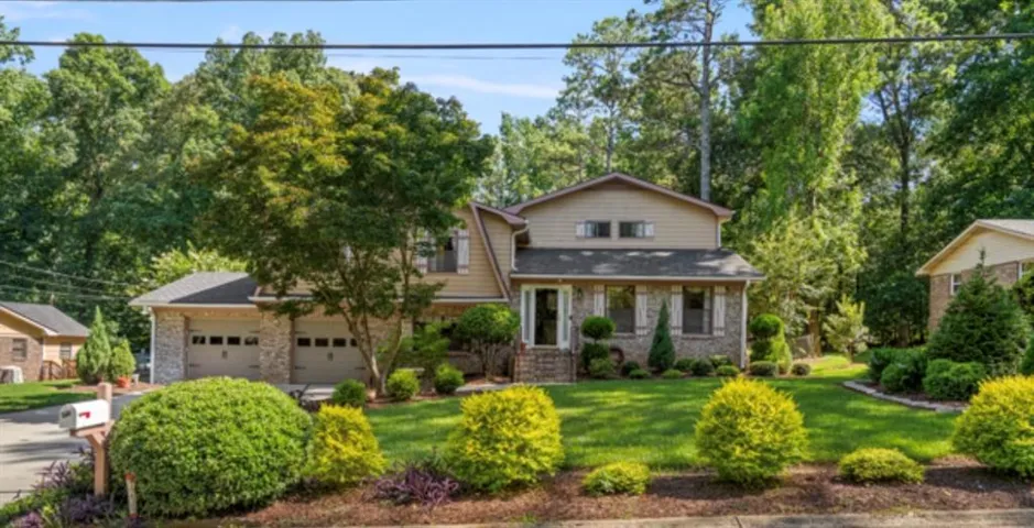 Two-story residence with a two-car garage, stone and siding exterior, front lawn, and mature landscaping