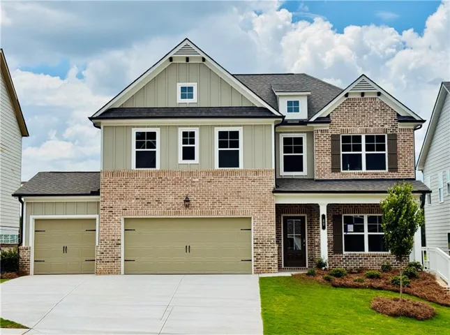 Brick and siding exterior with dark shutters, a covered porch entryway, and an attached two-car garage