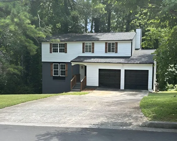 Split-level residence featuring a two-car garage with black doors, a dark gray lower exterior, and white siding on the upper level