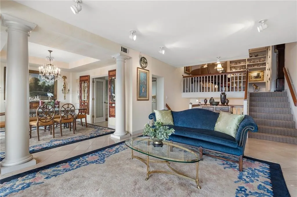 Tiled living room featuring decorative columns, visible vents, a raised ceiling, an inviting chandelier, and stairs