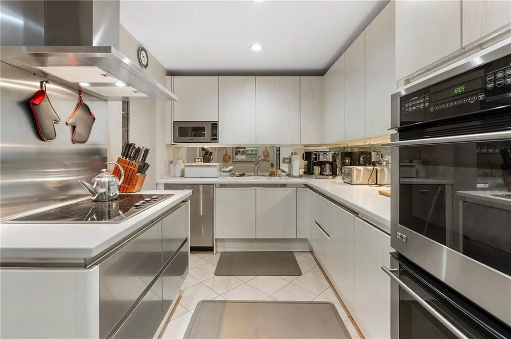 Kitchen with light tile patterned floors, light countertops, stainless steel microwave, electric stovetop, and wall chimney exhaust hood