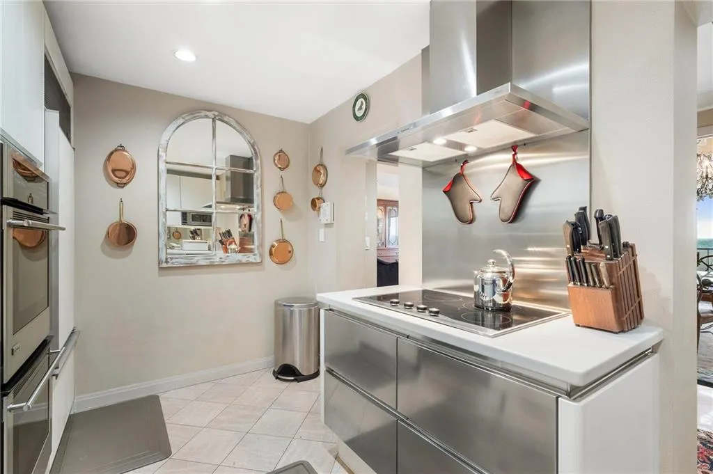 Kitchen with wall chimney exhaust hood, light countertops, oven, baseboards, and black electric cooktop