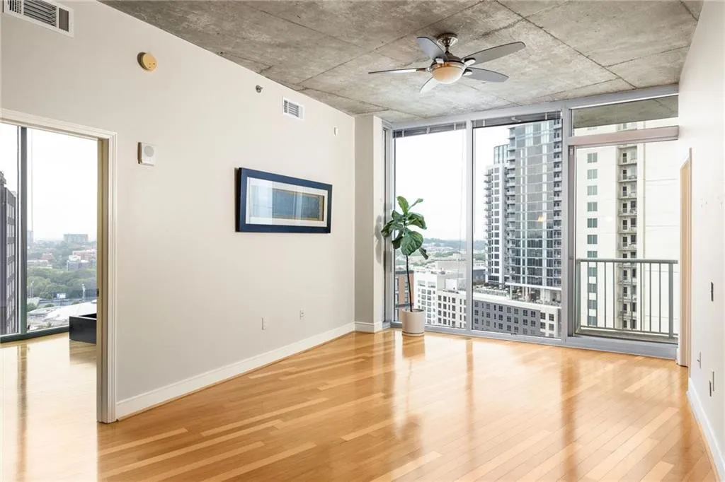 Empty room featuring wood finished floors, healthy amount of natural light, a ceiling fan, floor to ceiling windows, and a view of city