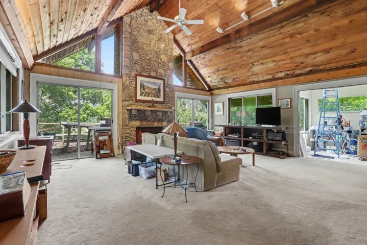 Distinctive architectural character, including soaring Vaulted Wood Ceilings, exposed beams, a dramatic Stone Fireplace, and walls of windows that take advantage of the private, wooded surroundings