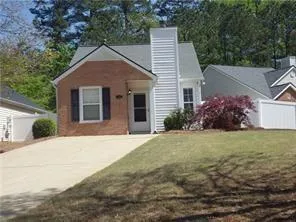 Brick and siding exterior featuring a prominent chimney, concrete driveway, and a front lawn with mature landscaping