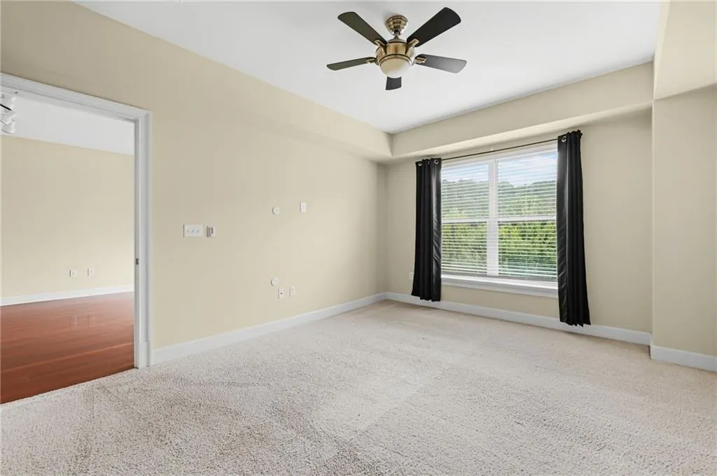 Large primary bedroom with neutral wall tones and neutral colored carpet, adjacent to custom closet system and bathroom.