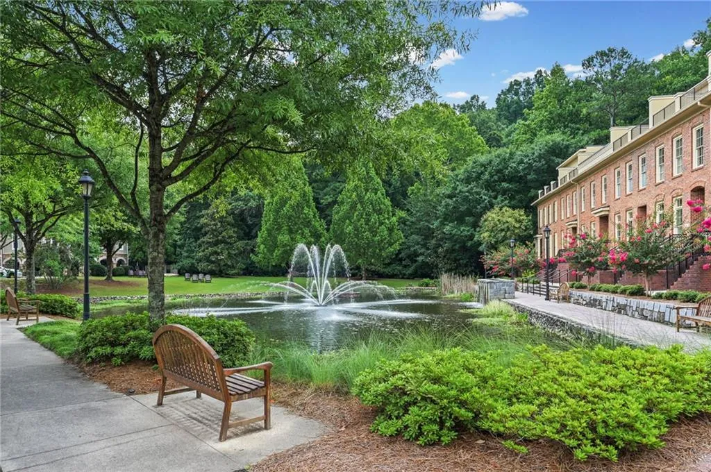 Community pond with a central fountain, bordered by a paved walkway and mature landscaping-Daylight View
