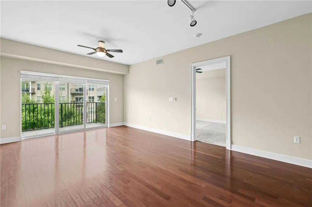 Spacious living area featuring wood-finish flooring, neutral paint, and access to a large balcony